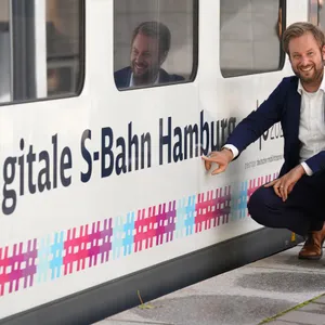 Anjes Tjarks (Bündnis 90/Die Grünen), Senator für Verkehr und Mobilitätswende, zeigt auf den Schriftzug „Digitale S-Bahn Hamburg“ an einer S-Bahn der Linie S2 am Bahnhof Bergedorf.