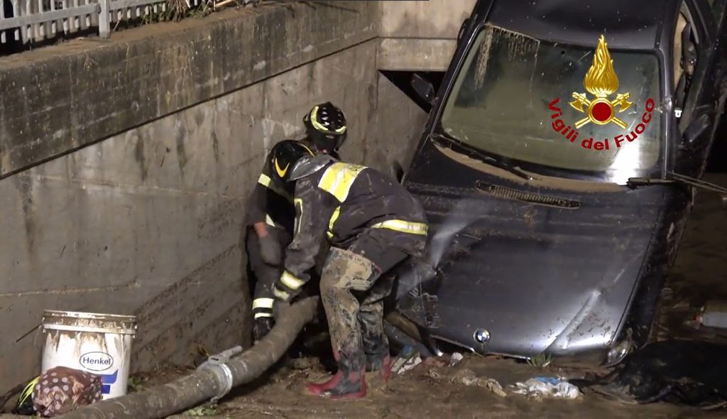 Feuerwehrleute schieben einen Schlauch in eine Tiefgarage, die durch ein angeschwemmtes Auto versperrt ist.