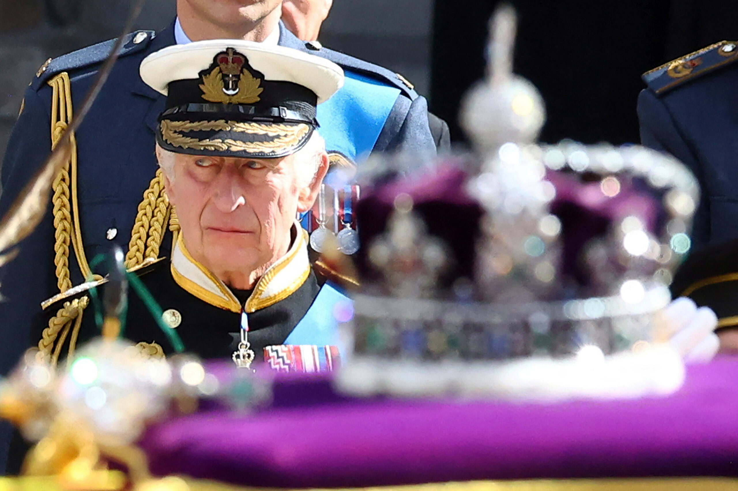 Charles steht hinter dem Sarg, auf dem eine lilafarbene Krone liegt