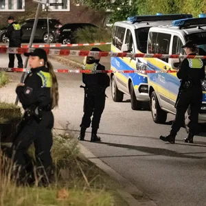 Polizisten und Einsatzfahrzeuge stehen in einem abgesperrten Bereich rund um den möglichen Tatort.