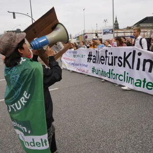 Ein Demonstrant hält ein Megaphon vor dem Mund und spricht zu den Teilnehmern hinter dem Banner "alle fürs Klima"