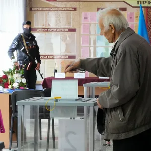 Ein Mann gibt seine Stimme in Luhansk unter der Beobachtung eines Bewaffneten ab.