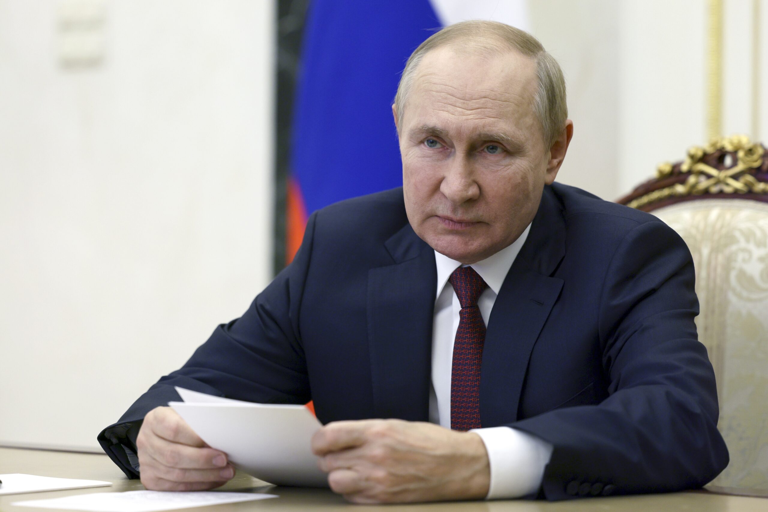 Putin sitzt an einem Tisch und hält Zettel in der Hand