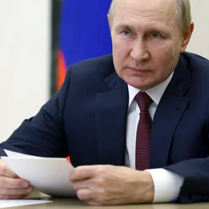 Putin sitzt an einem Tisch und hält Zettel in der Hand