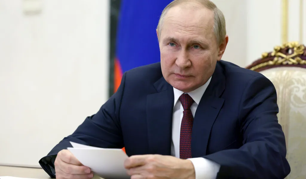 Putin sitzt an einem Tisch und hält Zettel in der Hand
