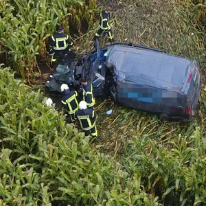 Feuerwehrkräfte stehen um einen Transporter, der in einem Feld neben einer Bundesstraße steht