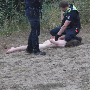 Ein Polizist legt einem nackten Mann Handschellen an