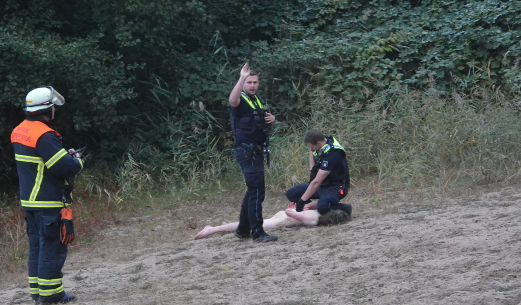 Ein Polizist legt einem nackten Mann Handschellen an