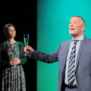 Michael Roll mit Sektglas in der Hand, im Hintergrund unscharf zwei Frauen