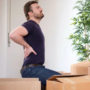 Ein Mann hält sich den Rücken vor Schmerzen, vor ihm Kisten