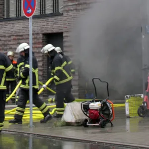 Dichter Rauch zieht aus einer Tiefgarage, vor der Feuerwehrkräfte stehen
