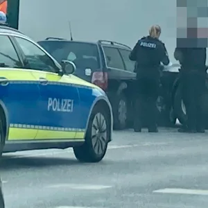 Polizisten stehen neben einem Auto, das unter einen Lkw geraten ist