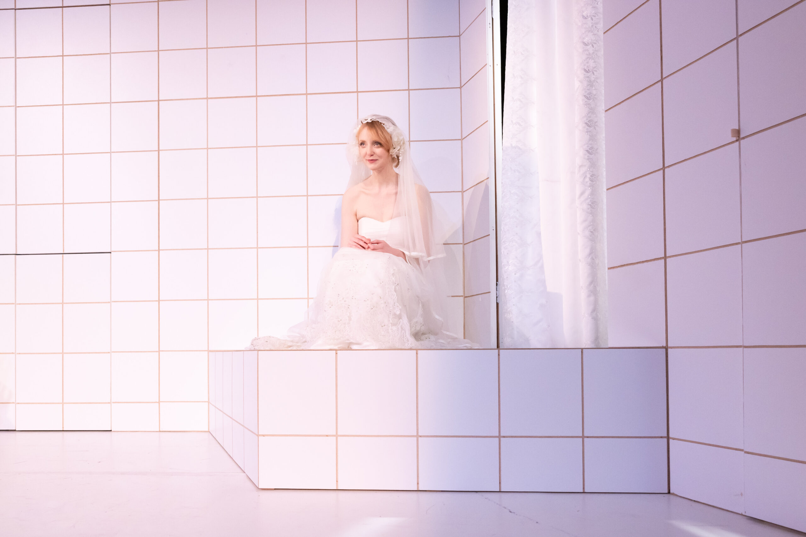 Frau im weißen Hochzeitskleid sitzt auf dem Boden eines komplett weiß gekachelten Raums