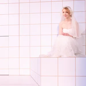 Frau im weißen Hochzeitskleid sitzt auf dem Boden eines komplett weiß gekachelten Raums