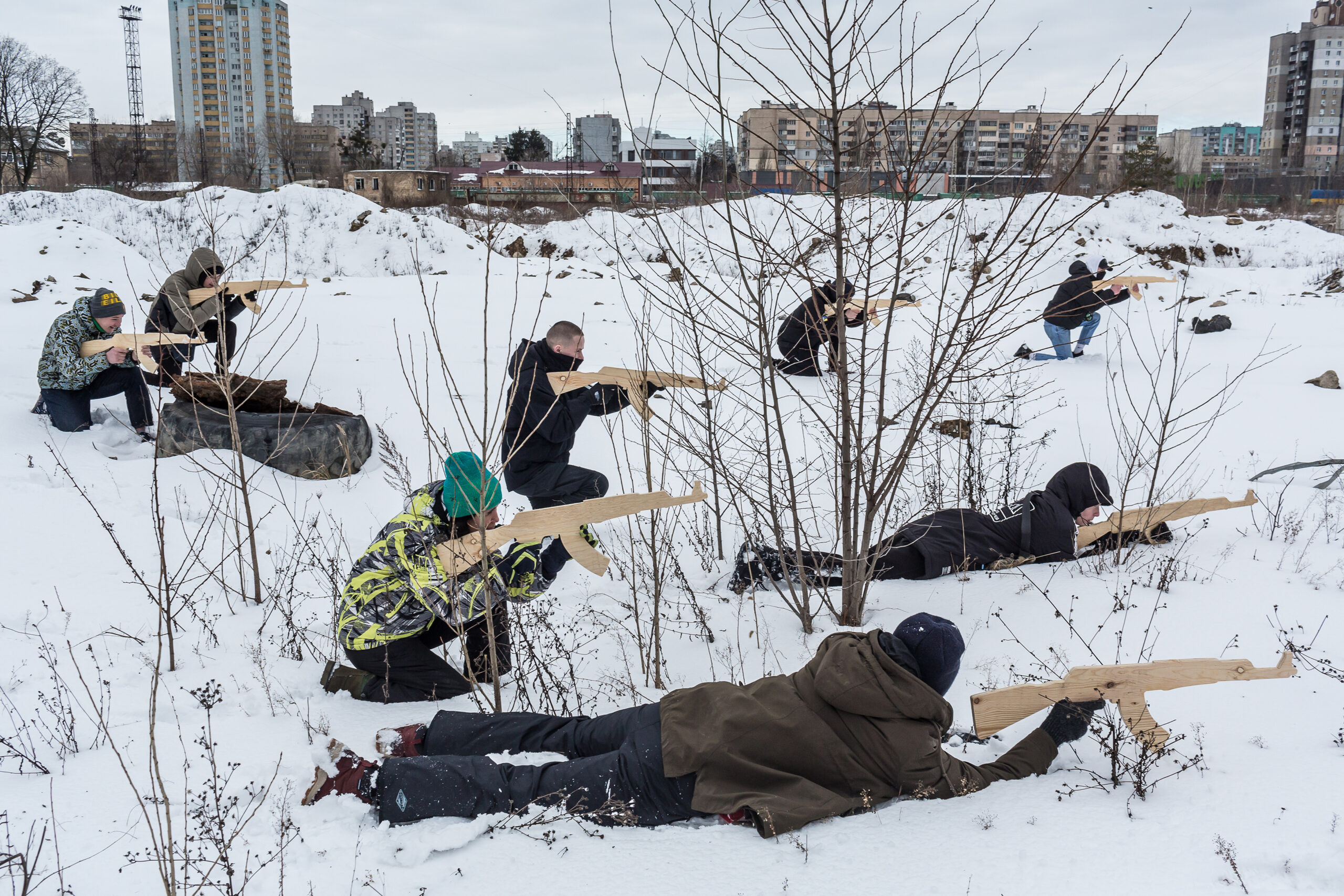 Menschen liegen im Schnee und zielen mit Holz-Waffen auf ein für uns nicht sichtbares Ziel