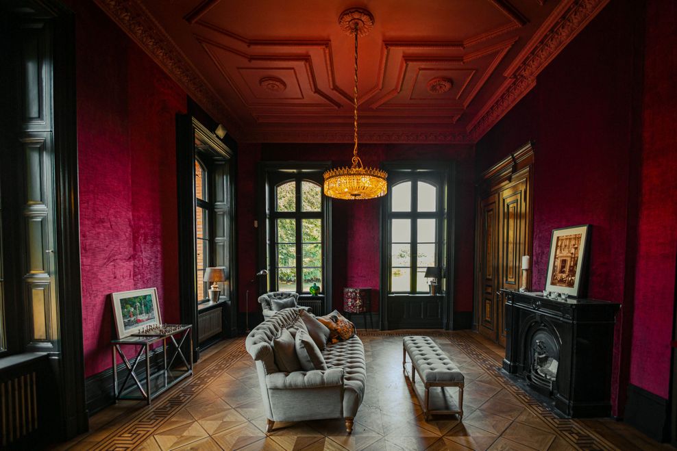 In der Bibliothek stehen ein Sofa, ein Kamin, Bücherregale und ein Tisch mit einem Schachspiel. Die Wände und Fensterrahmen sind dunkel, damit das Grün des Parks noch intensiver wirkt.