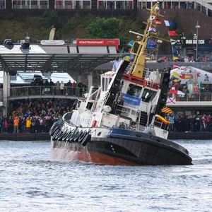 Schaulustige an den Landungsbrücken beobachten einen Schlepper beim traditionellen Schlepperballett auf der Elbe