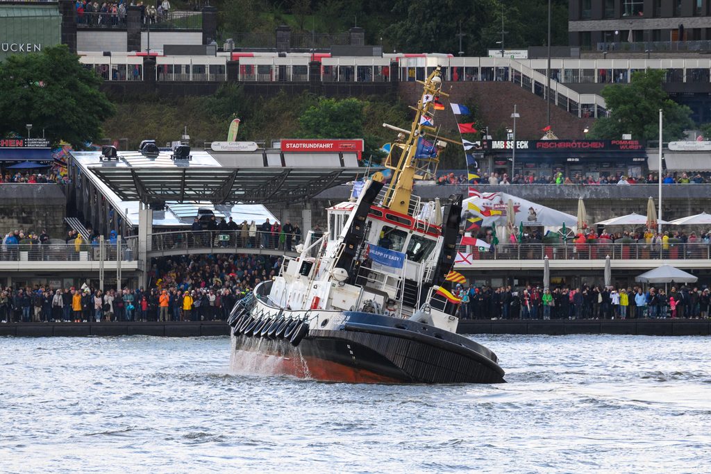 Schaulustige an den Landungsbrücken beobachten einen Schlepper beim traditionellen Schlepperballett auf der Elbe