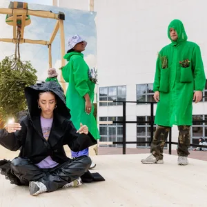 Künstler des Kollektivs „Baltic Raw Org“ präsentieren auf einem Laufsteg CO2-neutralisierende Kostüme. Während man in den Taschen des grünen Kostüms Pflanzen mit sich tragen kann, soll das mattschwarze Wärme aufnehmen und damit der Klimaerwärmung entgegenwirken.