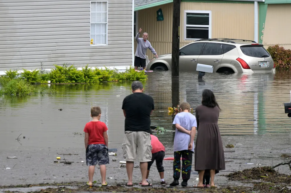Bewohner:innen eines überfluteten Viertels stehen vor Wassermassen.