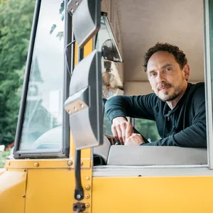 Lohrmann im Bus hinter dem Steuer, er schaut aus dem Seitenfenster