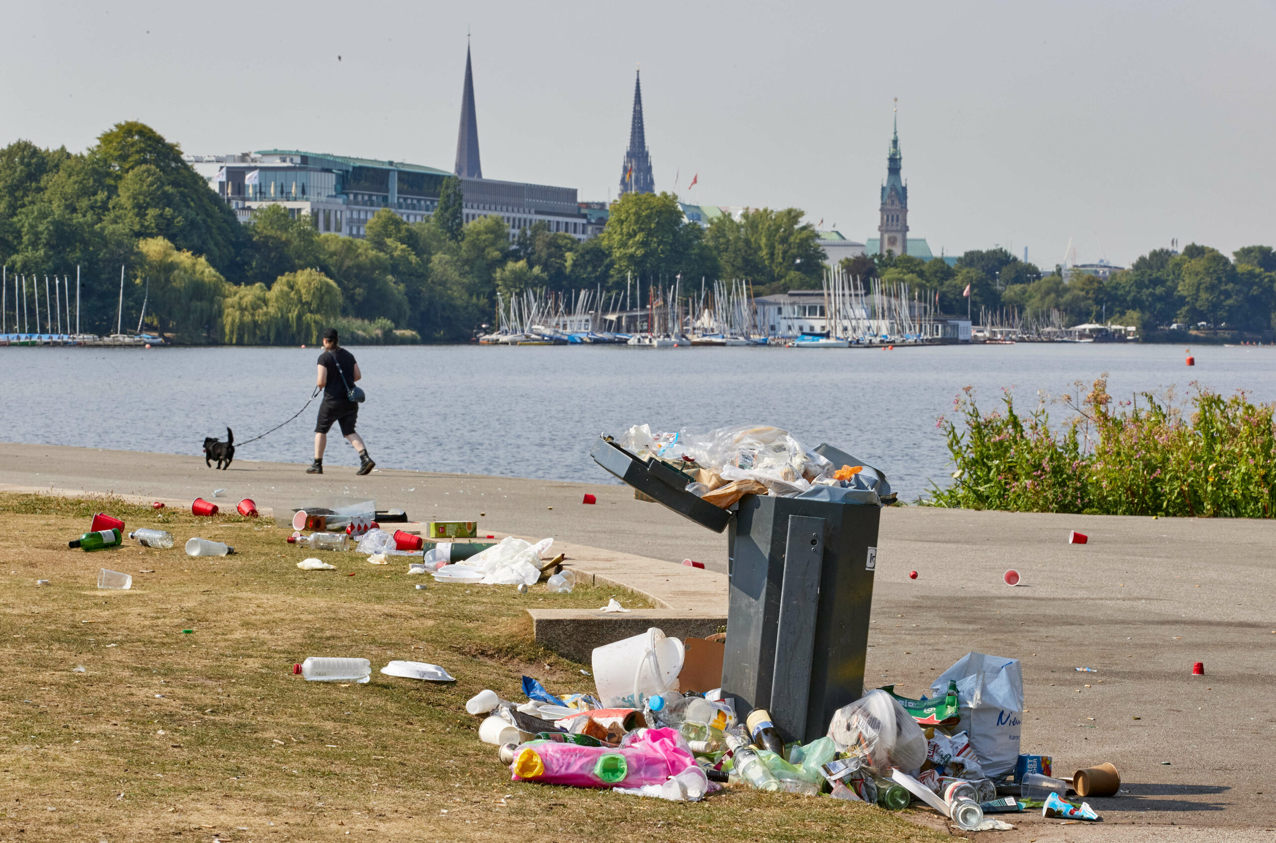 Müll liegt am Wiesenrand und auf dem Weg um einen überquellenden Mülleimer an der Alsterwiese Schwanenwik in Hamburg-Hohenfelde.