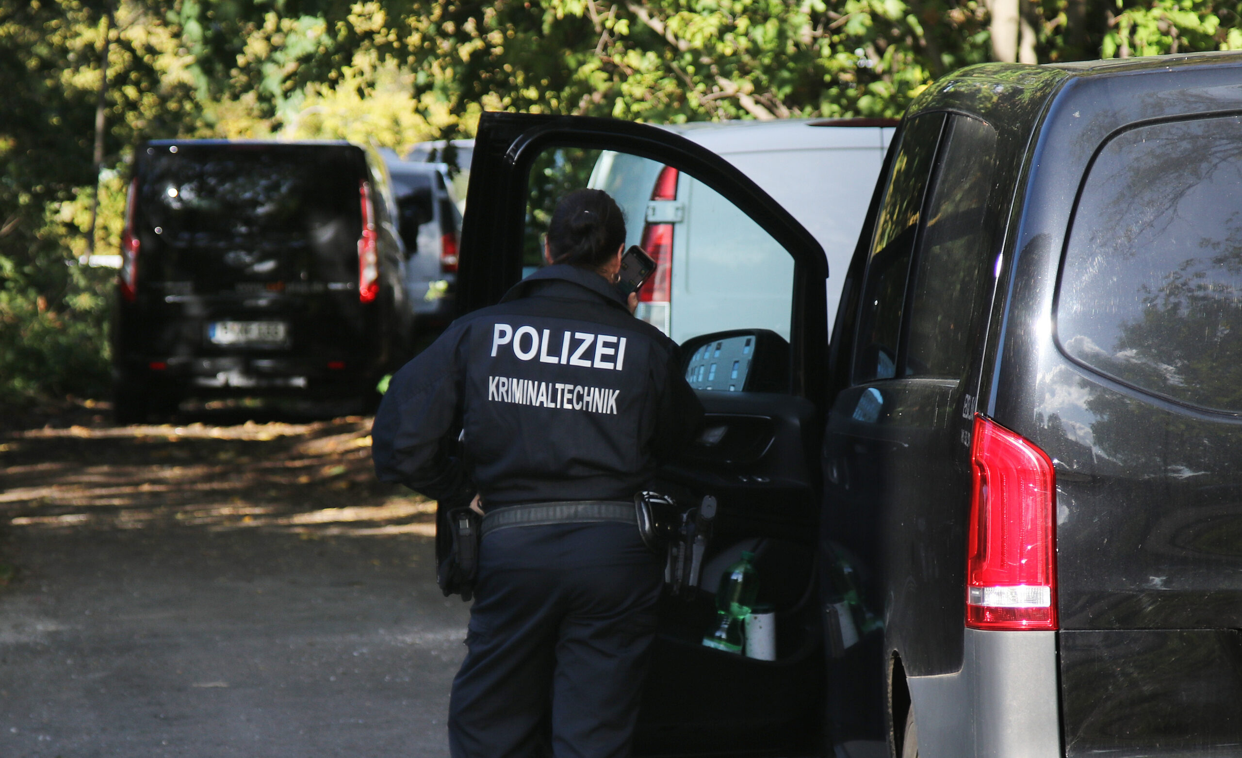 Eine Kriminaltechnikerin steht in der Nähe vom S-Bahnhof Hohenschönhausen in Berlin neben Fahrzeugen der Polizei.
