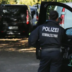 Eine Kriminaltechnikerin steht in der Nähe vom S-Bahnhof Hohenschönhausen in Berlin neben Fahrzeugen der Polizei.