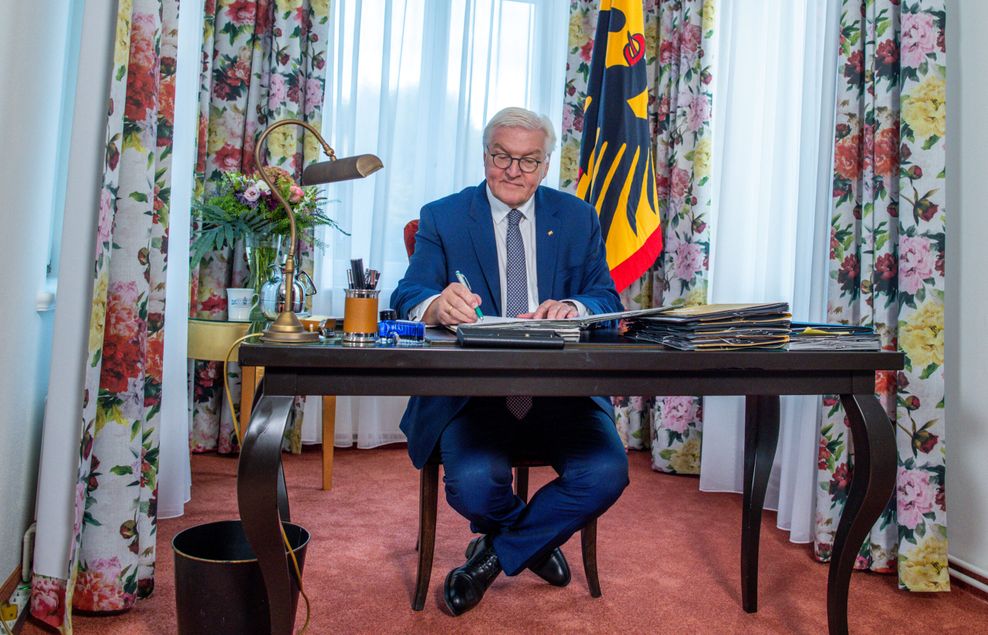 Bundespräsident Frank-Walter Steinmeier sitzt an einem Tisch und signiert ein Dokument