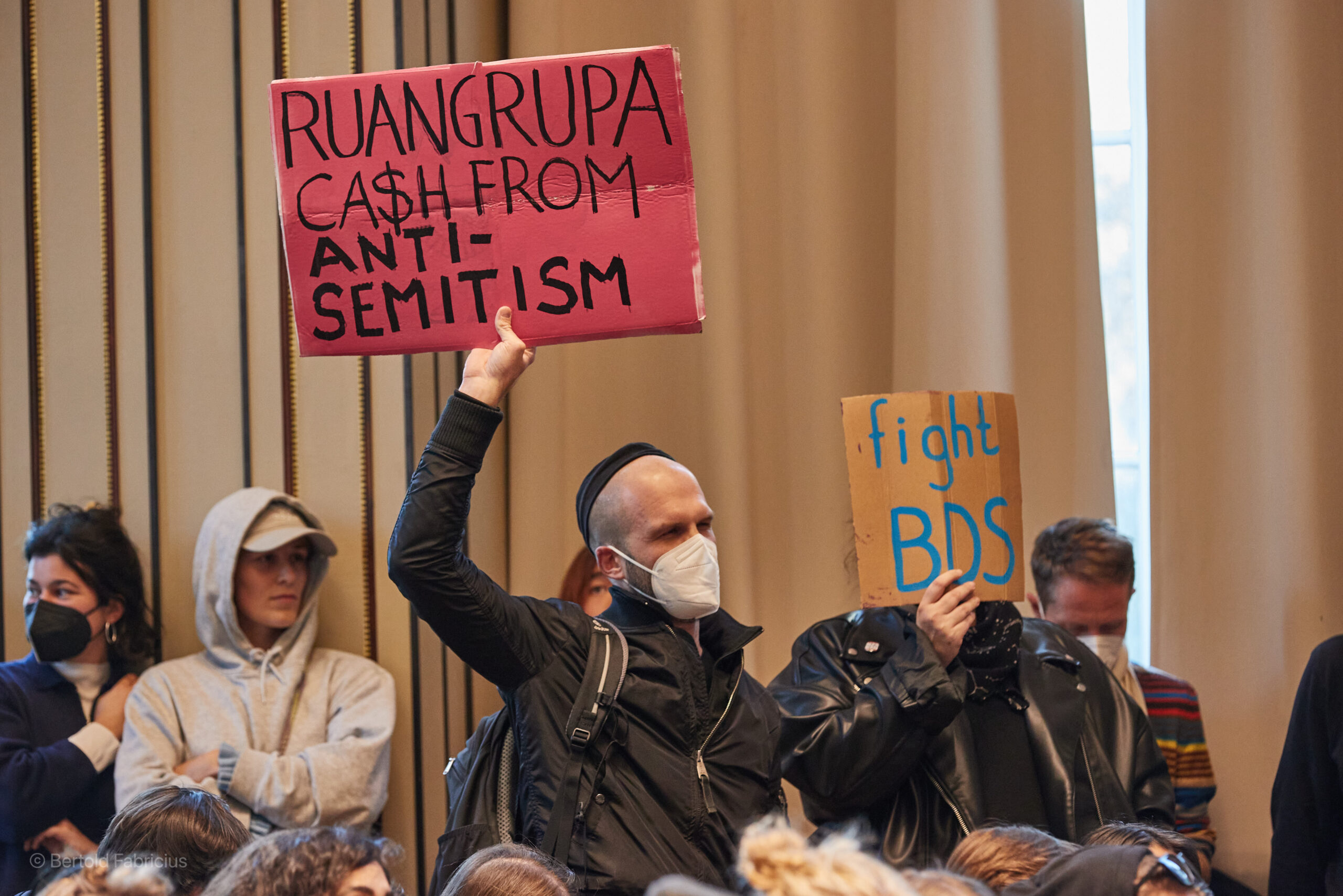 Protestierende halten in der Aula der HFBK Transparente mit der Aufschrift „Ruangrupa Ca$h From Antisemitism“ und „Fight BDS“ hoch.