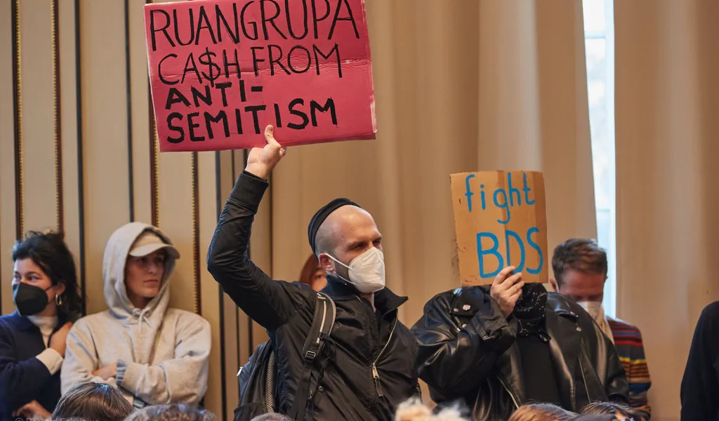 Protestierende halten in der Aula der HFBK Transparente mit der Aufschrift „Ruangrupa Ca$h From Antisemitism“ und „Fight BDS“ hoch.