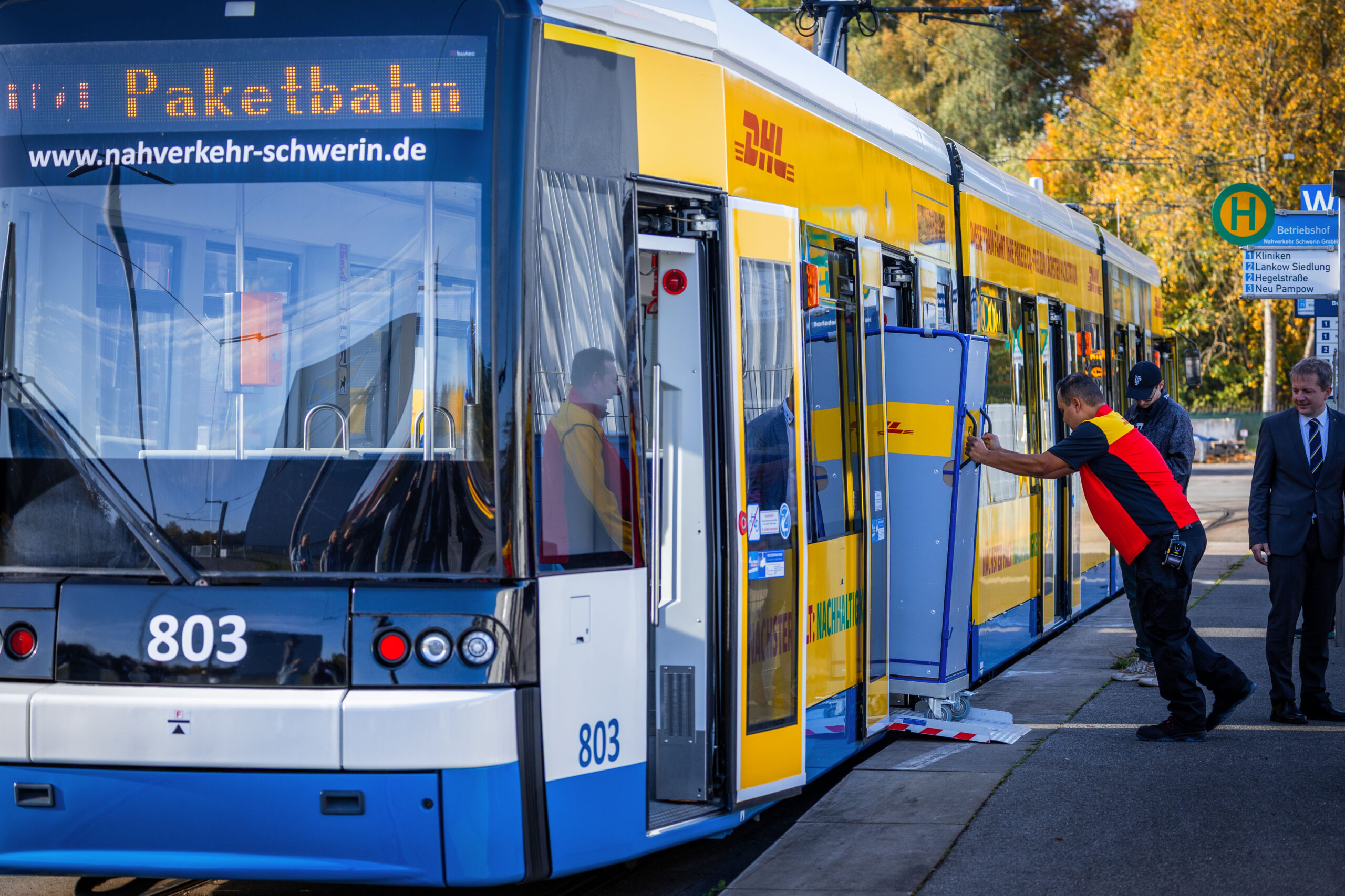 Ein Mitarbeiter der Deutschen Post schiebt einen Transportwagen für Pakete in eine Straßenbahn des Schweriner Nahverkehr.