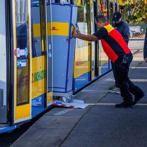 Ein Mitarbeiter der Deutschen Post schiebt einen Transportwagen für Pakete in eine Straßenbahn des Schweriner Nahverkehr.