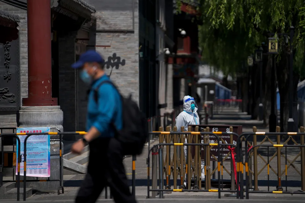 Ein Mann in Schutzkleidung bewacht Absperrungen vor geschlossenen Läden in Peking.