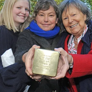 Susanne Friedburg (M.) hält mit ihrer Tochter Mirabelle und ihrer Großtante Gesa Ohle den Stolperstein für Auguste Friedburg.