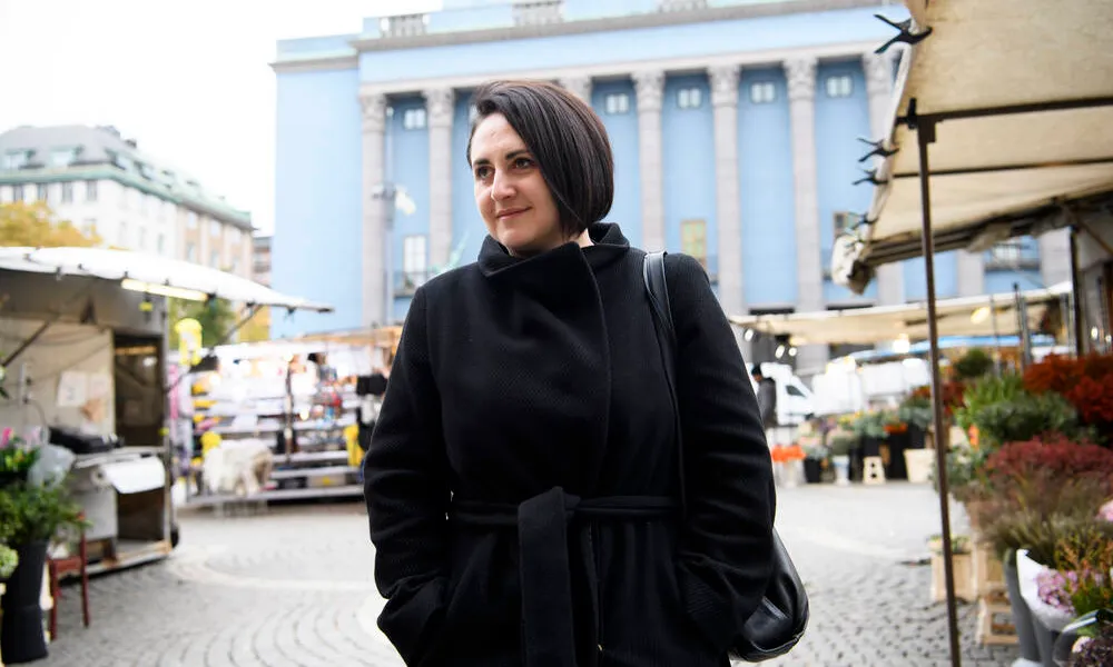 Die Autorin trägt einen schwarzen Mantel und steht auf einem Markt in Stockholm