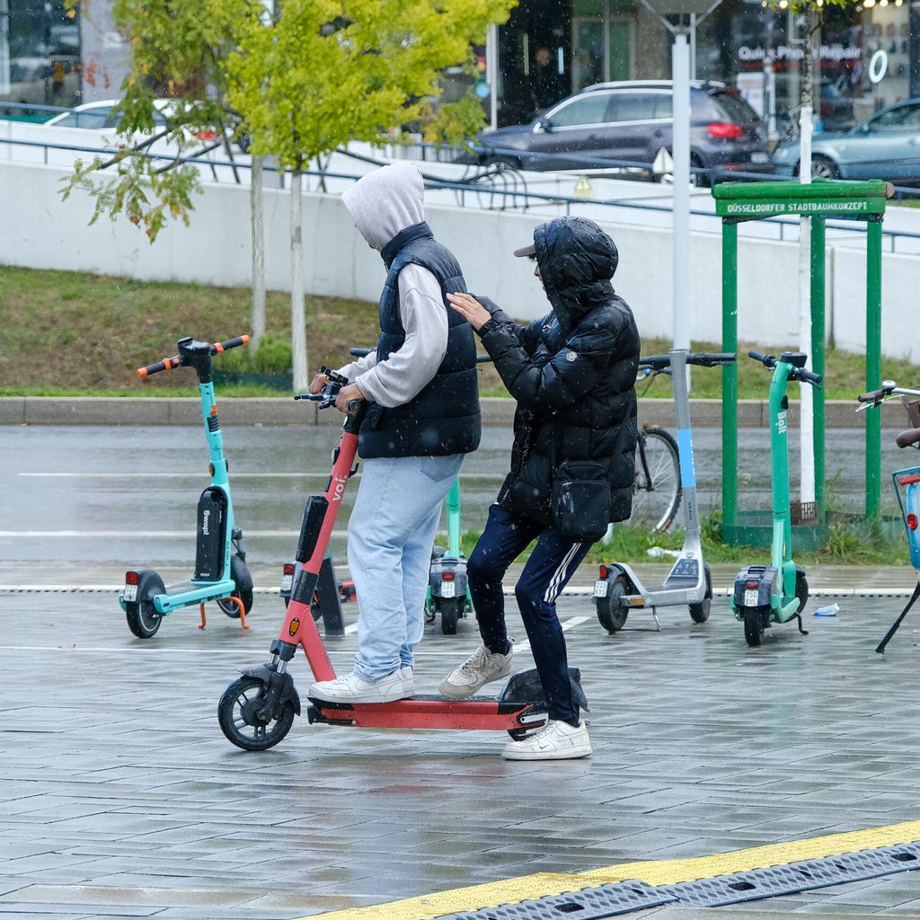 Zwei Jugendliche fahren auf einem E-Scooter.