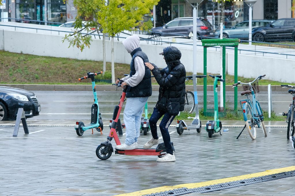 Zwei Jugendliche fahren auf einem E-Scooter.