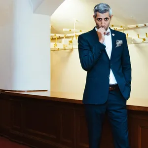 Michel Abdollahi trägt Anzug und steht vor einer leeren Theater-Garderobe