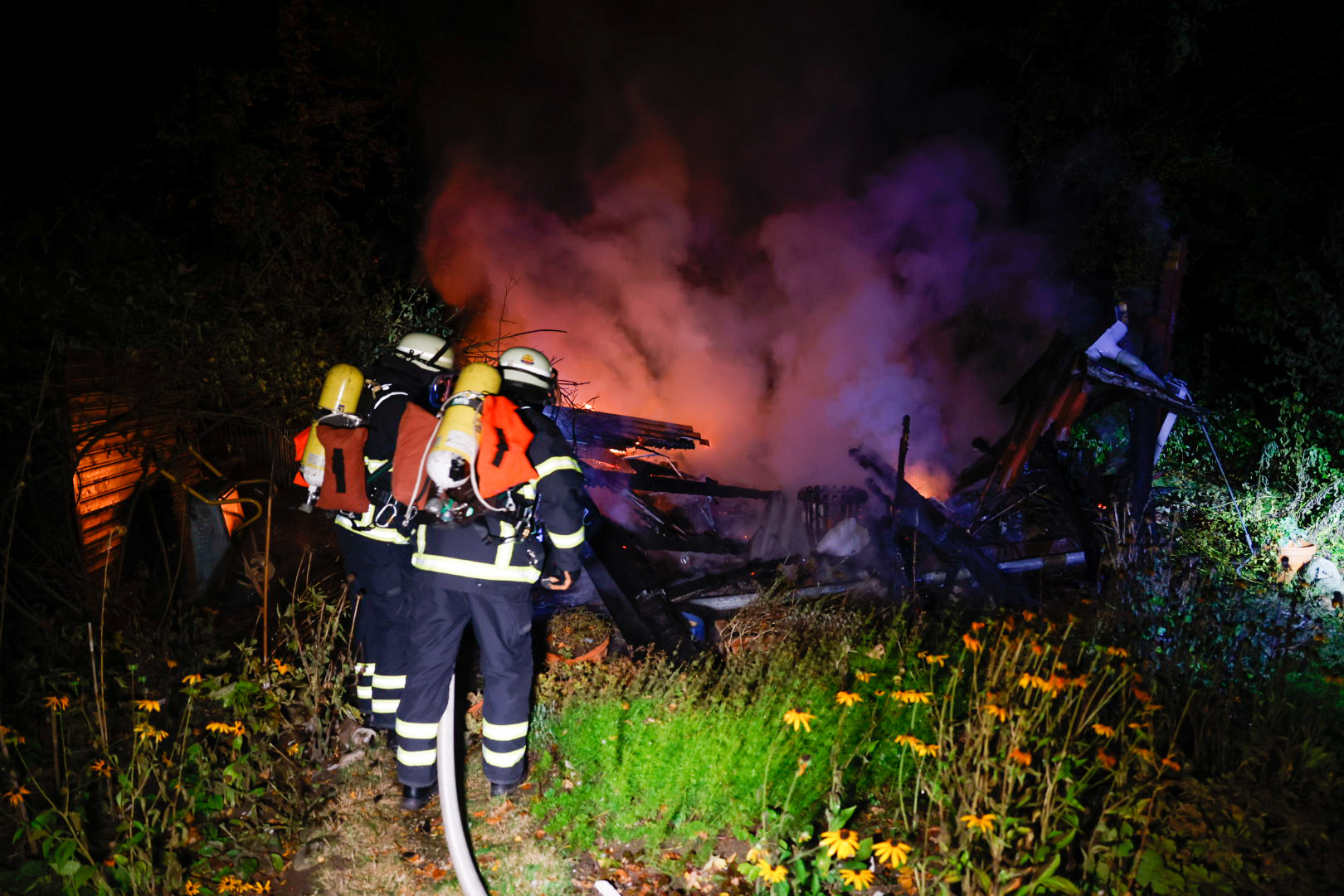 Einsatzkräfte löschen die brennenden Überreste der Laube.