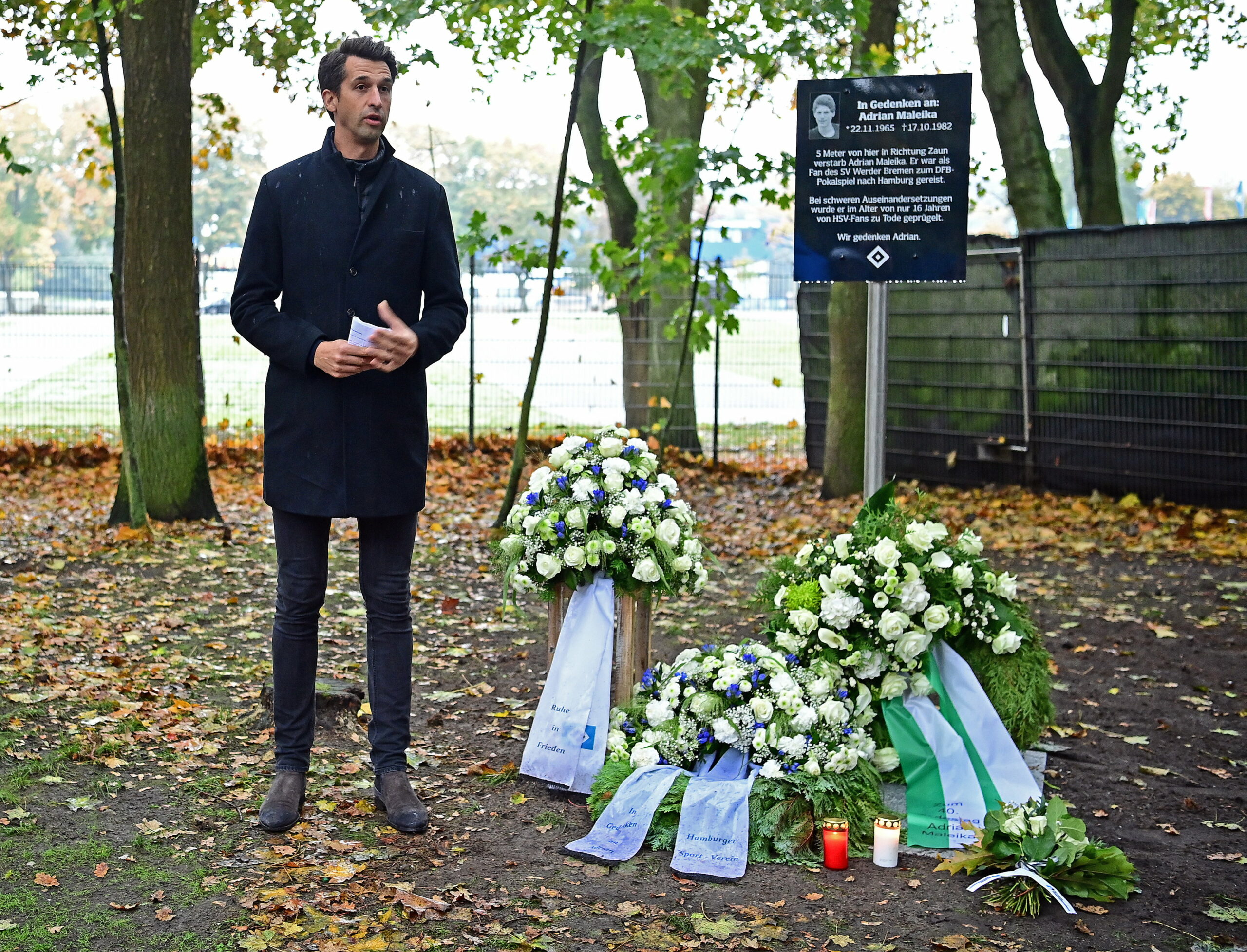 HSV-Vorstand Jonas Boldt steht neben einer Gedenktafel und Trauerkränzen für den getöteten Werder-Fan Adrian Maleika