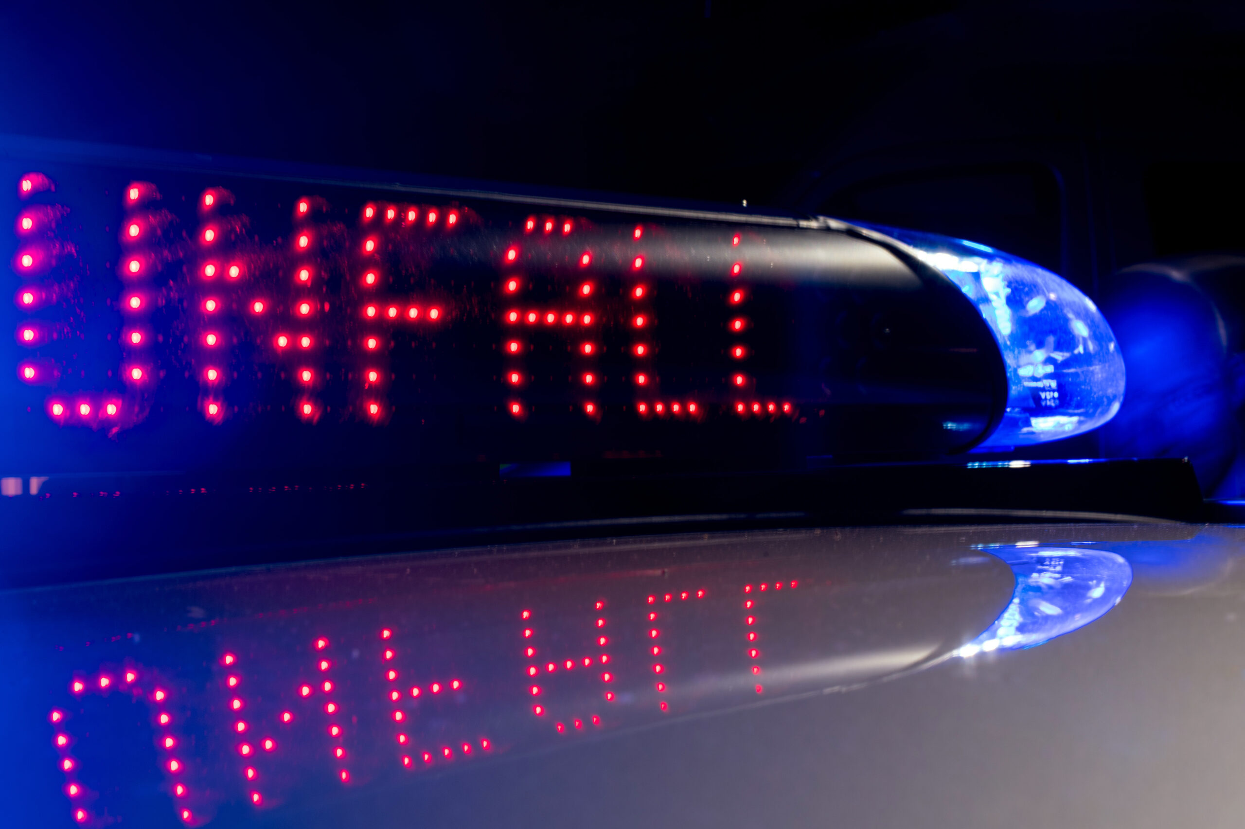 Das Blaulicht auf einem Fahrzeug der Polizei leuchtet in der Dunkelheit, während auf dem Display der Hinweis "Unfall" zu lesen ist