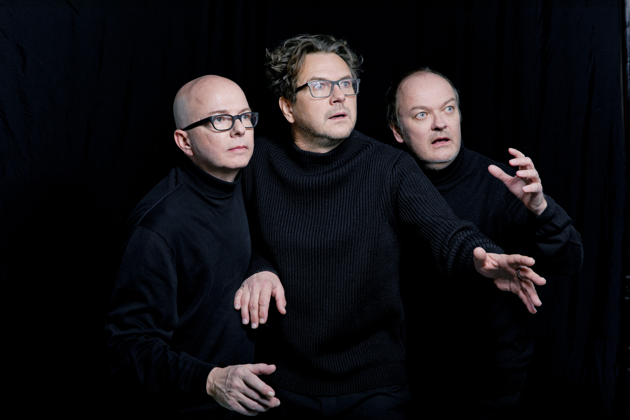 Drei Männer in schwarzen Pullovern vor schwarzem Hintergrund