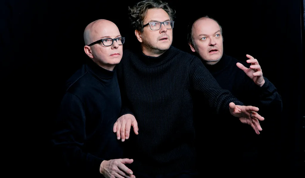 Drei Männer in schwarzen Pullovern vor schwarzem Hintergrund