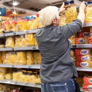Eine Mitarbeiterin von Edeka füllt ein Regal mit Nudeln auf.