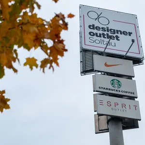 Ein Schild des Designer Outlets. Nike, Starbucks und Esprit-Schilder sind zudem zu sehen.