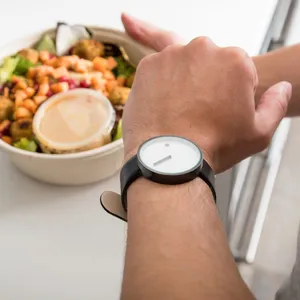 Mann schaut auf seine Uhr und hat einen Teller Essen in der anderen Hand.