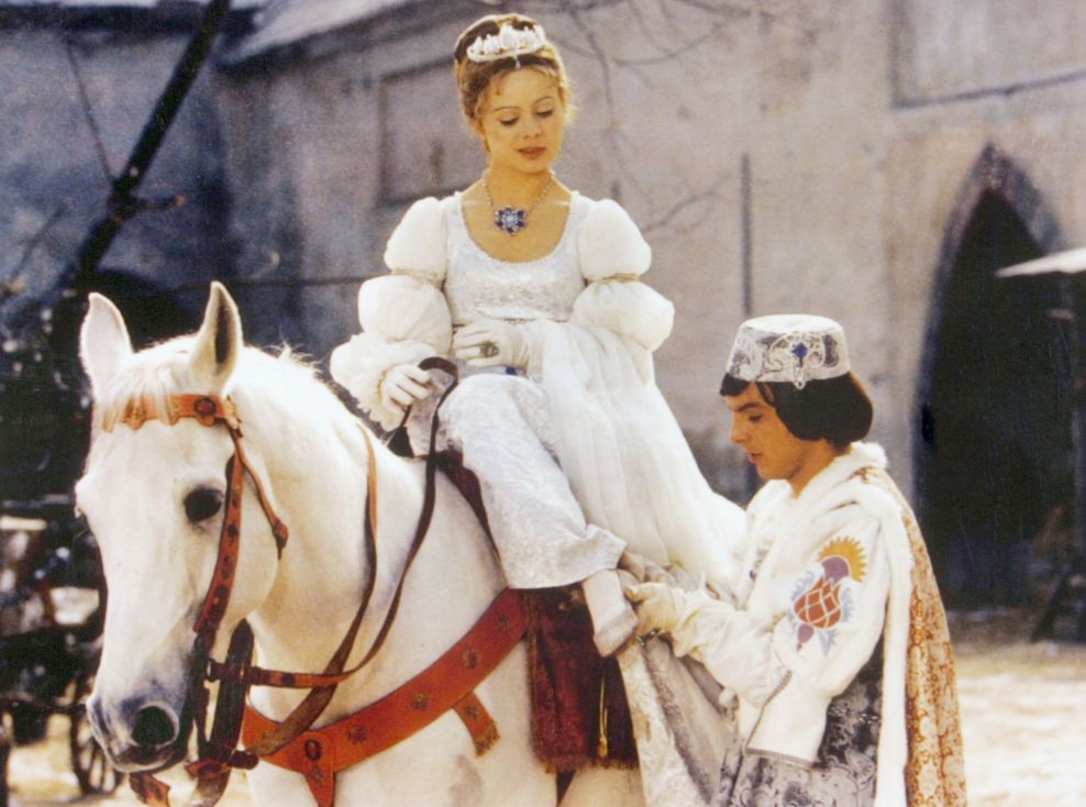 Der Prinz zieht Aschenbrödel den Schuh an. Das Mädchen sitzt auf einem weißen Pferd.