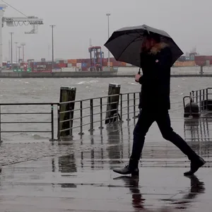 Ein Passant geht bei Regen und Wind an der Elbe entlang. (Archivbild)