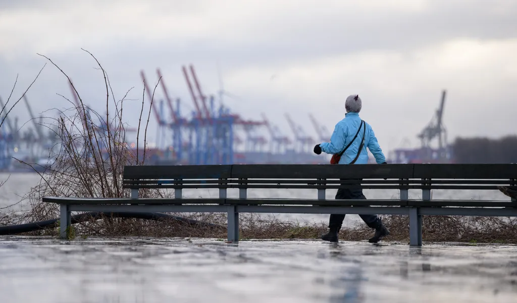 Eine Frau spaziert an der Elbe dick angezogen entlang